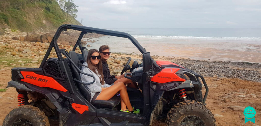 Pareja sonríe a cámara montados en un buggy frente al mar de Asturias