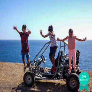 Tres niños saltan contentos junto a un buggy en Fuerteventura, Canarias